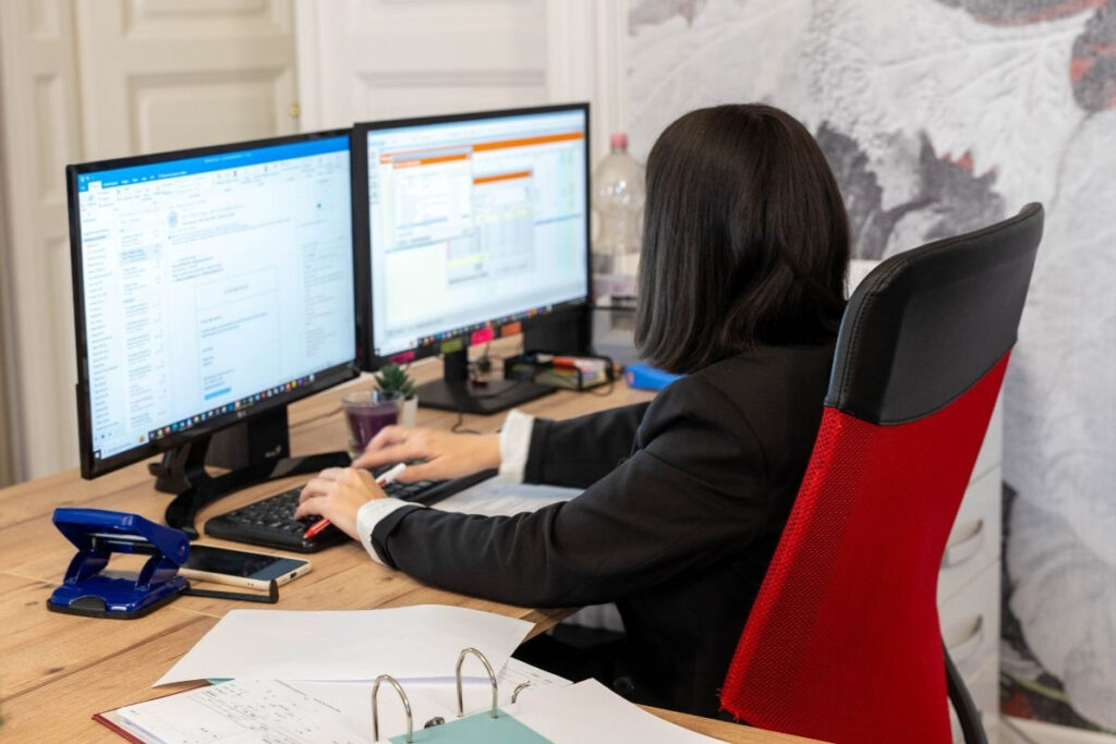 Könyvelő irodai környezetben, két monitor előtt dolgozik könyvelőszoftverrel és e-mailekkel