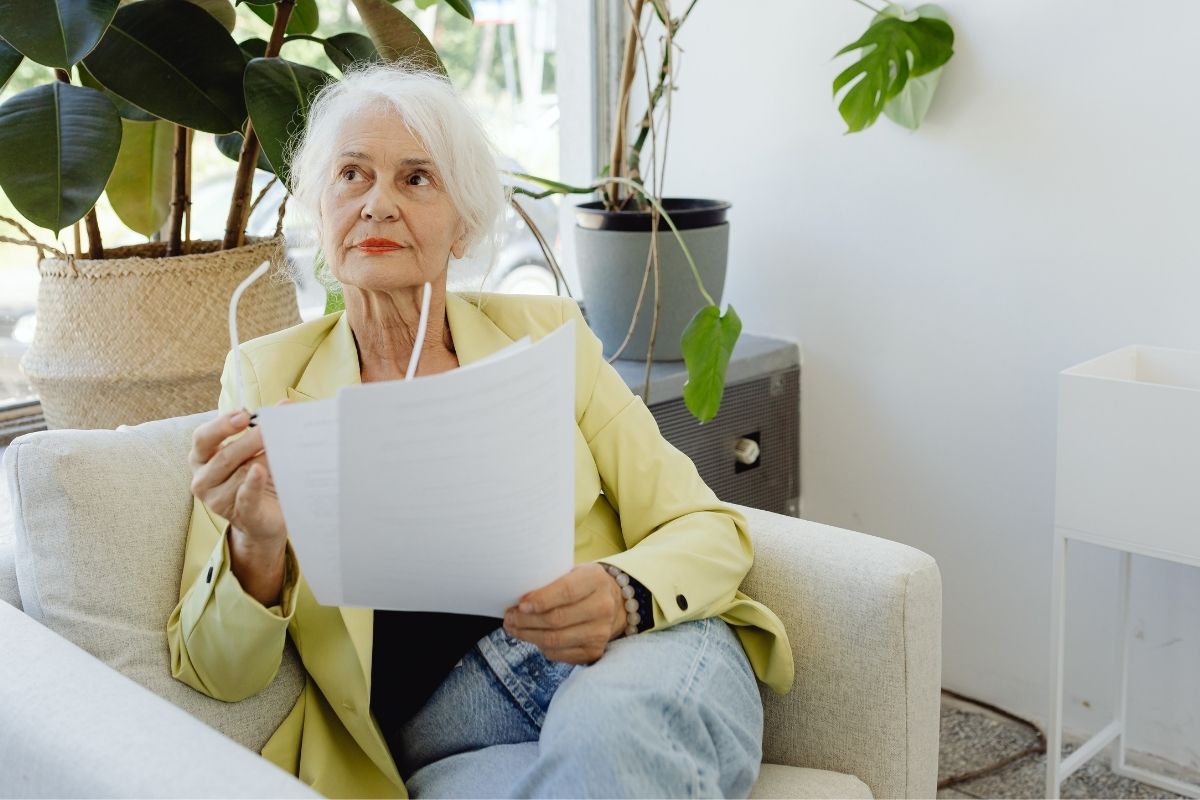 Idős könyvelő hölgy dokumentumokkal a kezében, döntést készít elő az értékátadásról.